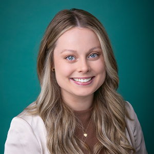 Female physician assistant smiling in front of teal blue photo backdrop.