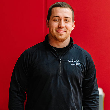 Male athletic trainer posing in front of a red background.