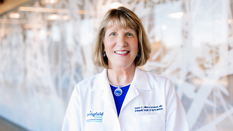 Woman smiling in front of a clear wall with a white tree decal.
