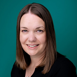 Nurse practitioner smiling in front of teal blue photo backdrop.