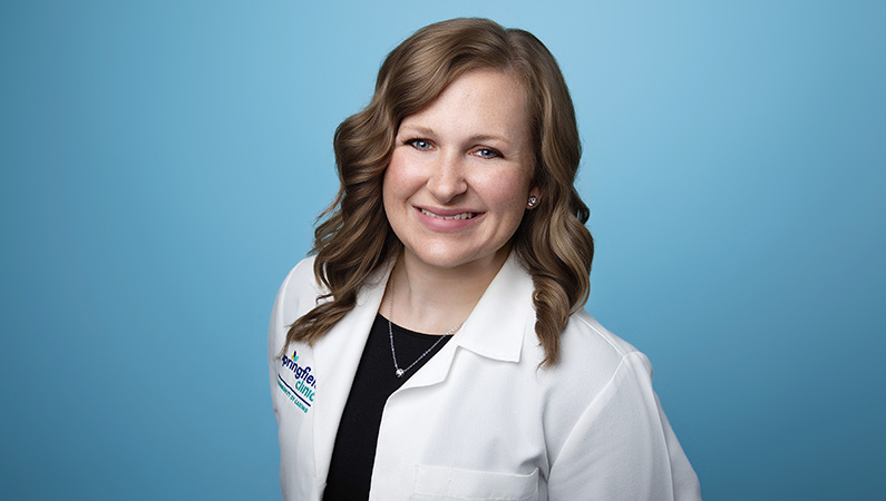 Female nurse wearing smile medical coat smiling in front of blue background