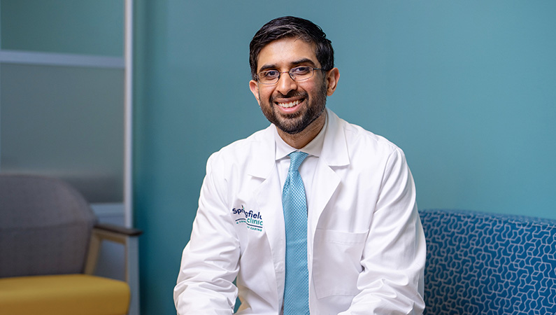 Male physician wearing white medical coat smiling in front of blue background