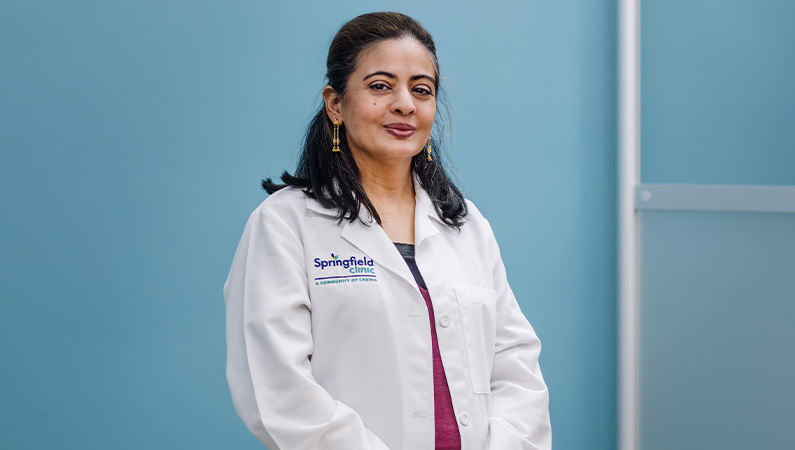 Female doctor with dark hair smiling in a while medical coat.