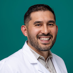 Male family medicine physician smiling in front of blue photo backdrop.