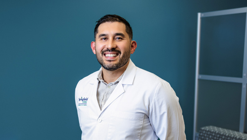 Male family medicine physician wearing white medical coat smiling.