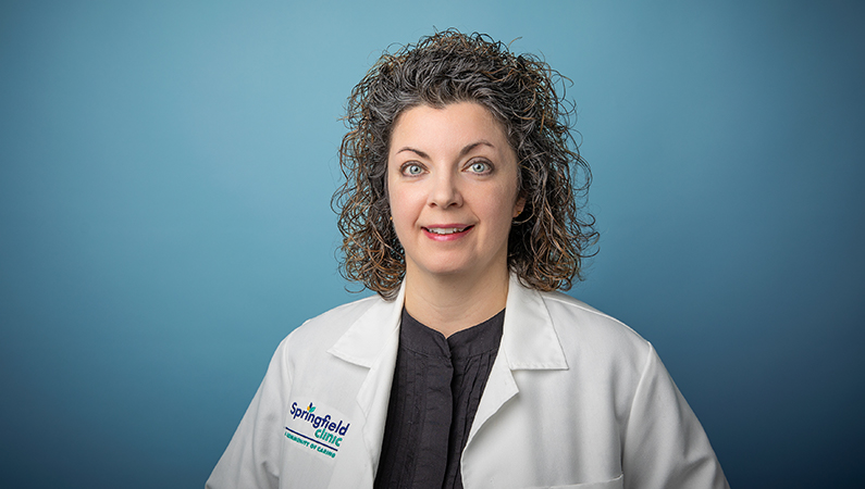 Female trauma surgeon wearing white medical coat smiling in professional headshot.