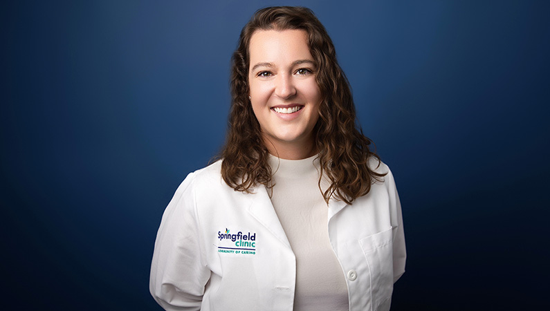 Female smiling in professional looking headshot with blue photo backdrop