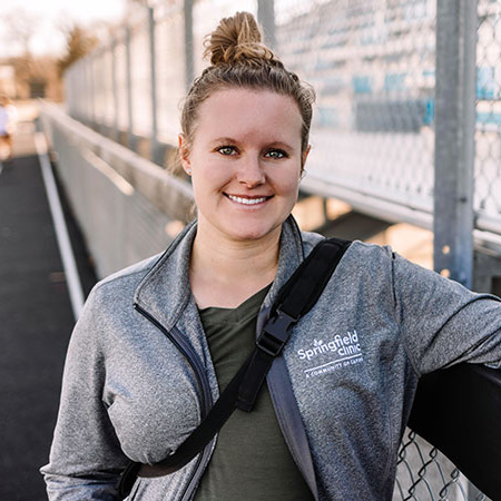 Female athletic trainer smiling on an outdoor track.