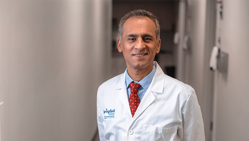 Male cardiologist wearing white medical coat smiling.