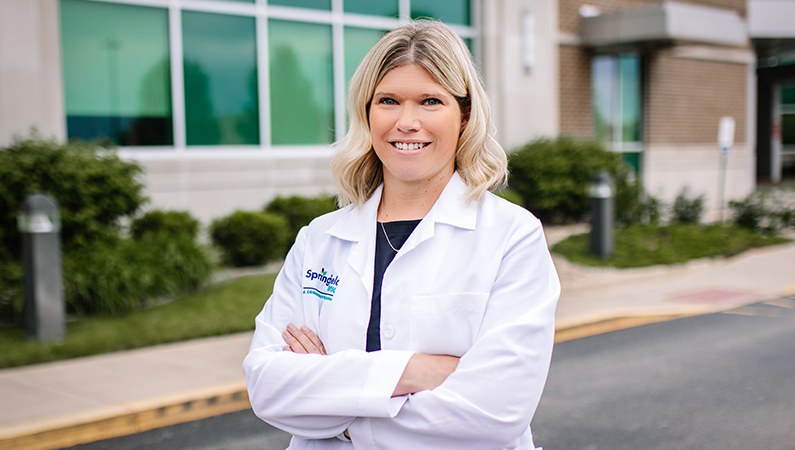 Female with light hair wearing white medical coat smiling in outdoor setting