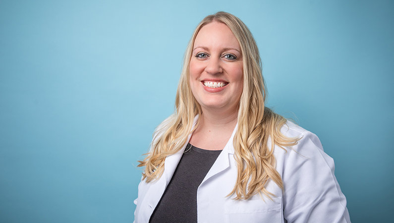 Female radiology doctor in white lab coat smiling in front of a light blue backdrop.