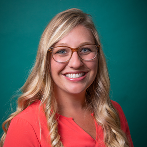 Female nurse practitioner professional headshot in front of a teal blue backdrop.