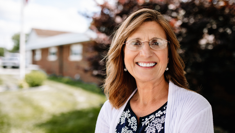 Woman smiling outside in front of a brick doctor's office and tree.