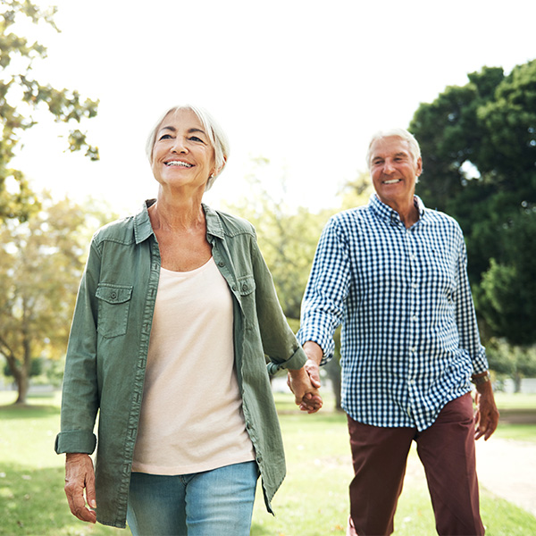 Elderly female and male holding hands while walking in an outdoor park setting.