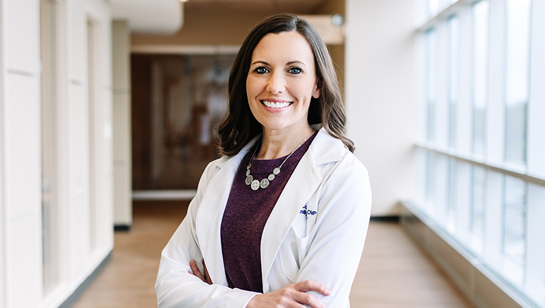 Female with dark hair wearing white medical coat smiling in a well-lit hallway