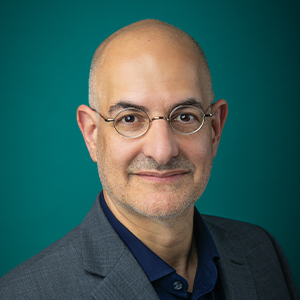 Male ophthalmologist smiling in front of a teal blue backdrop.