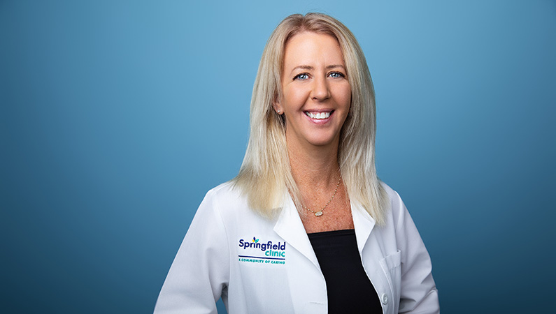 Female wearing white medical coat smiling in front of blue background