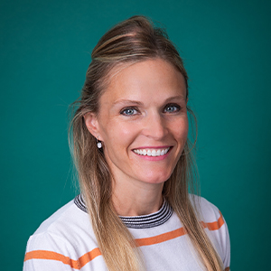 Female pediatrician smiling in front of a teal blue backdrop.