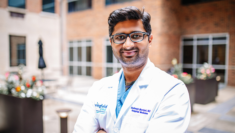 Male wearing glasses and white medical coat posing in lobby area
