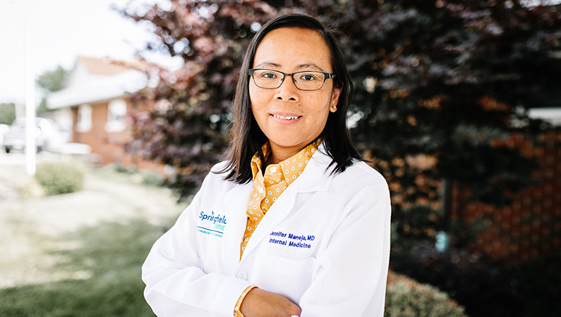 Female internal medicine doctor in white coat smiling outside.