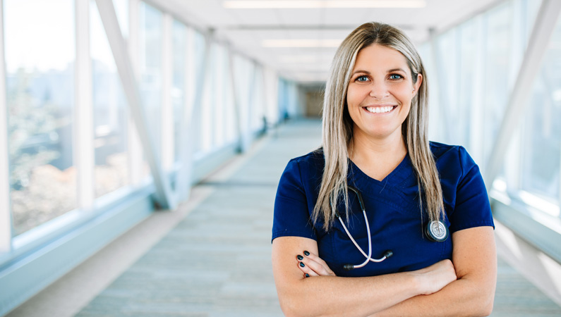 Female nurse in naturally lit hallway smiling.