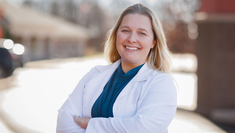 Female provider in white medical coat smiling in outdoor setting.