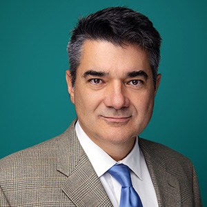 Male cardiology physician smiling in front of teal blue backdrop.