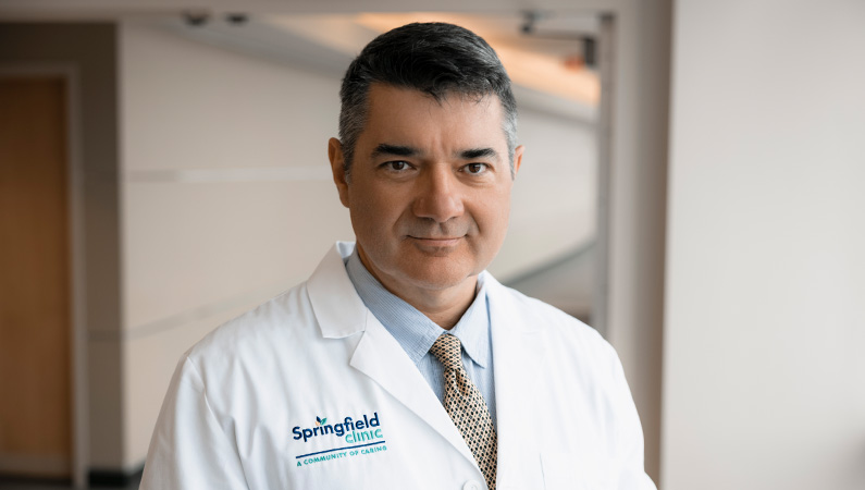 Male cardiologist wearing white medical coat smiling.