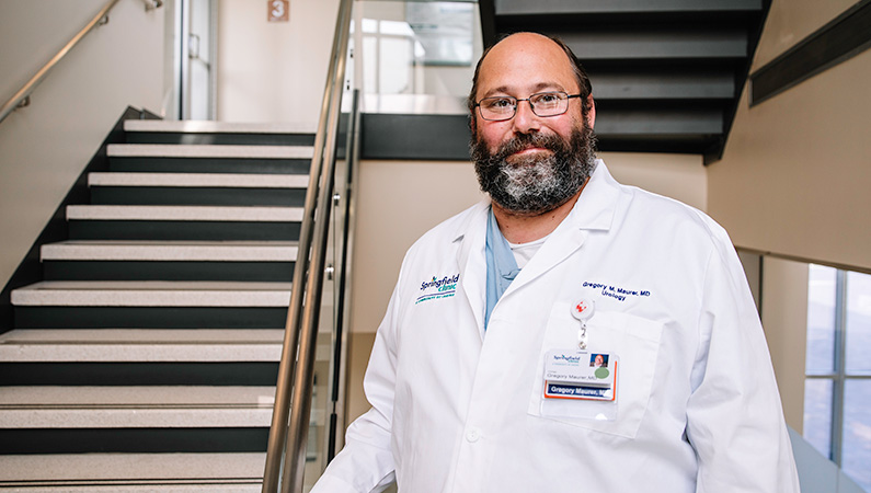 Man in a white doctors coat smiling in a well lit stairwell