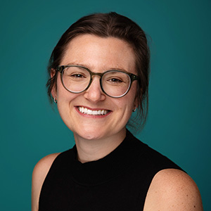 Female women's health physician smiling in front of teal photo backdrop.
