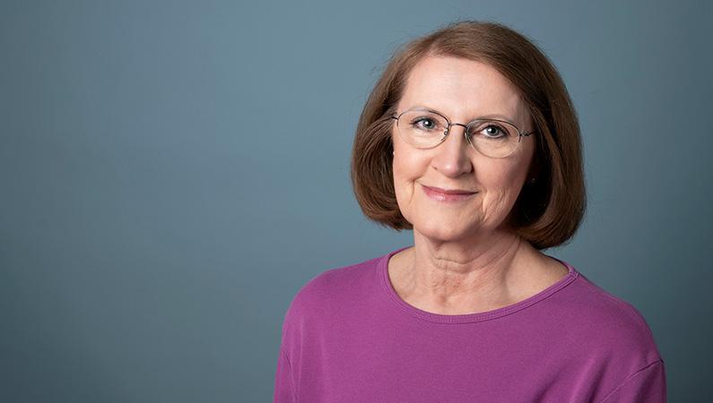Female with short brown hair and glasses smiling in front of studio lit gray backdrop