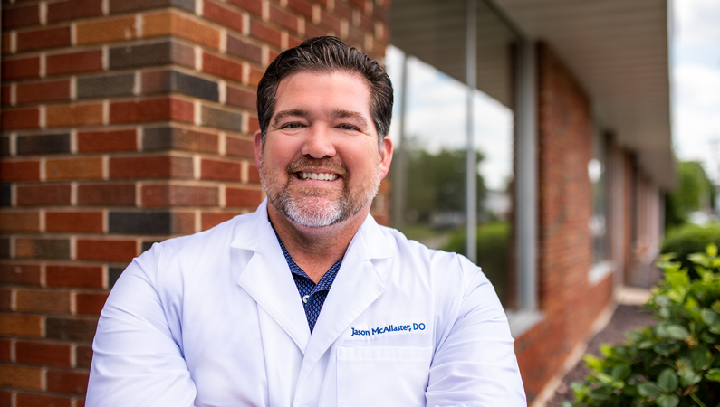 Male wearing white medical coat smiling in outdoor setting