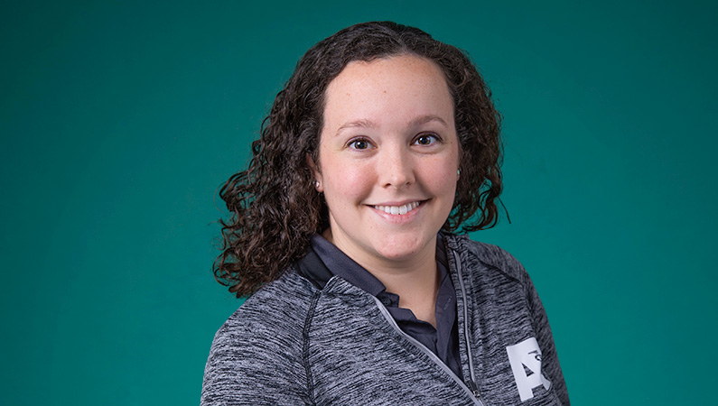 Female with short curly dark hair smiling in front of green background