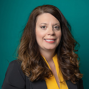 Female nurse practitioner professional headshot in front of a teal blue backdrop.