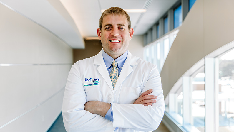 Male wearing white medical coat smiling in hallway setting