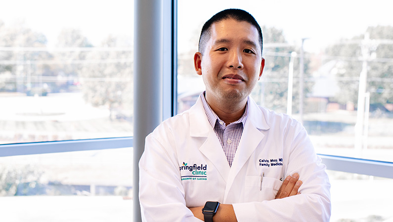 Man wearing a white doctors coat smiling in front of the window.