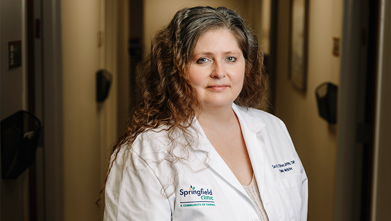 Female family medicine nurse practitioner in white coat smiling in a doctor's office hallway.