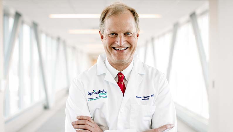 Urology doctor in white coat smiling in a naturally lit hallway.
