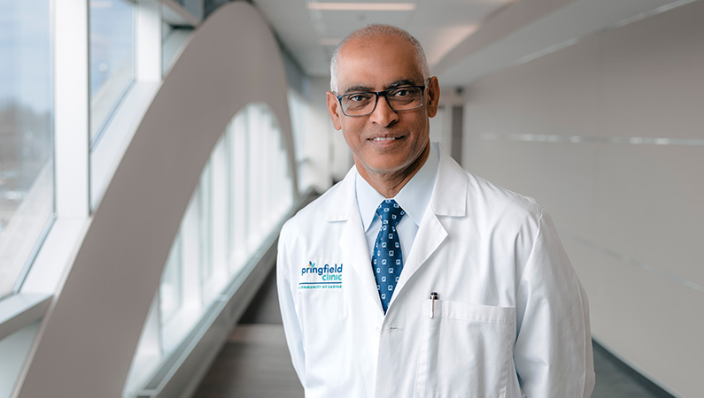 Male cardiologist wearing white medical coat smiling.