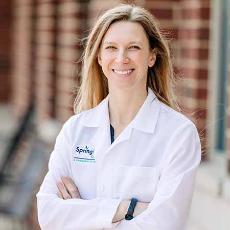 Female dermatology doctor in white coat smiling in an outdoor setting.