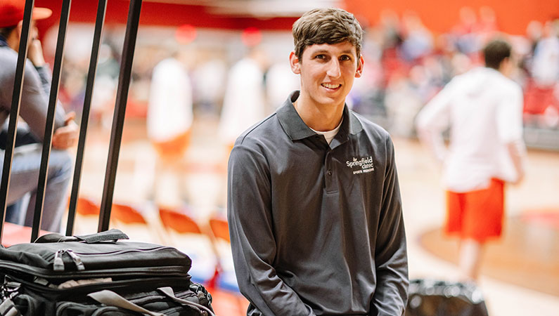 Male athletic trainer smiling with basketball court in background