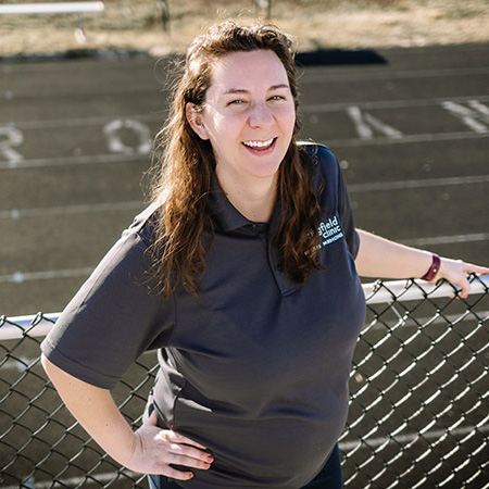 Female athletic trainer smiling with outdoor track in background.