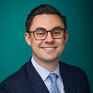 Male surgeon smiling in front of blue photo backdrop.
