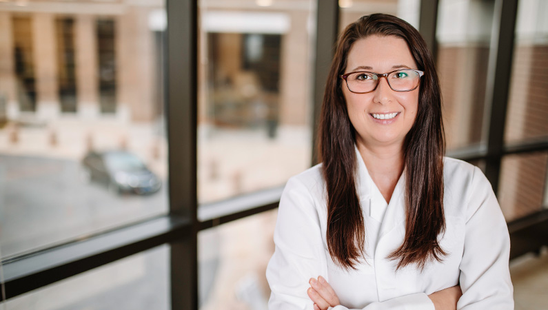 Woman wearing a white doctors coat standing in front of a window.