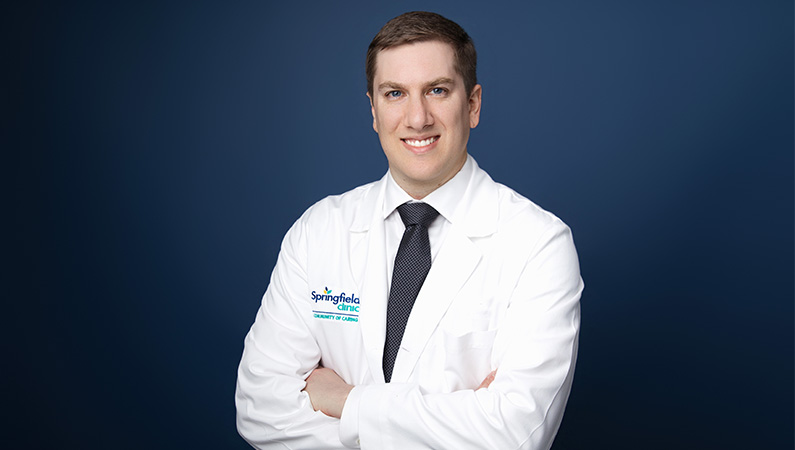 Douglas Onuscheck, MD, wearing white medical coat smiling in front of blue background