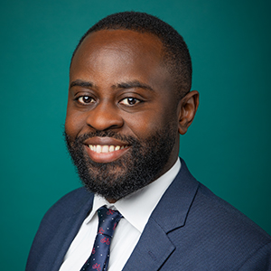 Male radiologist smiling in front of teal photo backdrop.