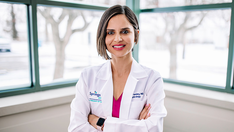 Woman wearing a white doctors coat, smiling in front of window