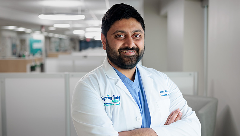 Male trauma surgeon wearing white lab coat smiling in a medical office.