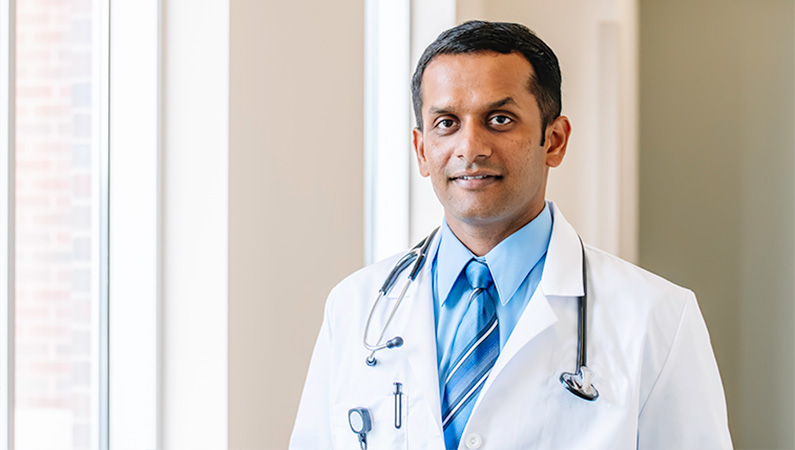 Man wearing a stethoscope around his  neck, smiling in front of a window.