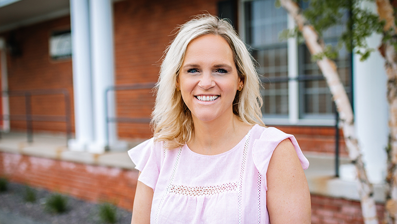 Woman smiling outside in front of the brick doctors office.